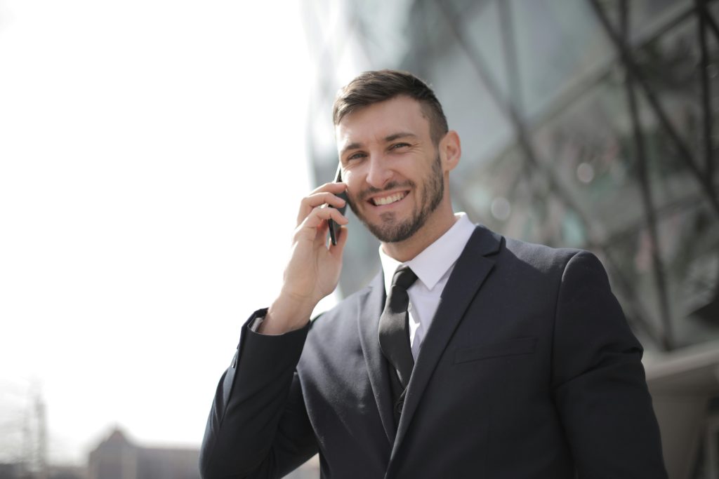 Smiling businessman in a suit having a phone call outside a modern glass building.